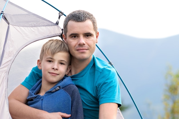 Vader met zijn kindzoon die samen in een tent in de zomerbergen rusten. Actief gezinsrecreatieconcept.