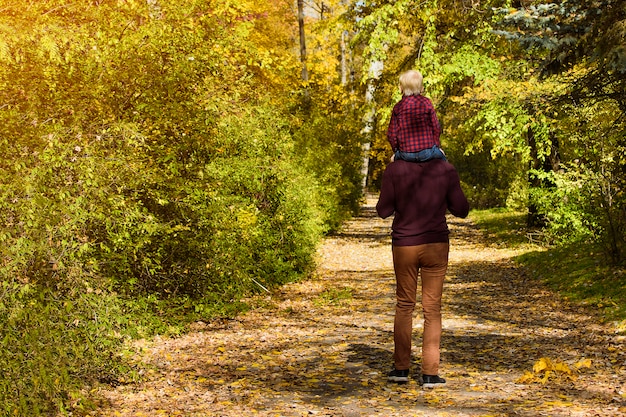 Foto vader met zoon die op zijn schouders in het de herfstbos loopt.