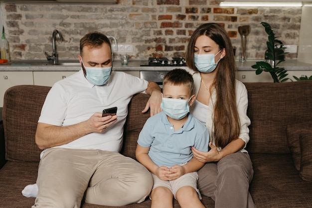 Vader, moeder en hun zoon zitten met medische gezichtsmaskers op een bank om verspreiding van coronavirus te voorkomen (COVID-19)