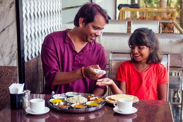 Vader, moeder en klein meisje die handdesinfecterende gel gebruiken voor het eten in het café van india