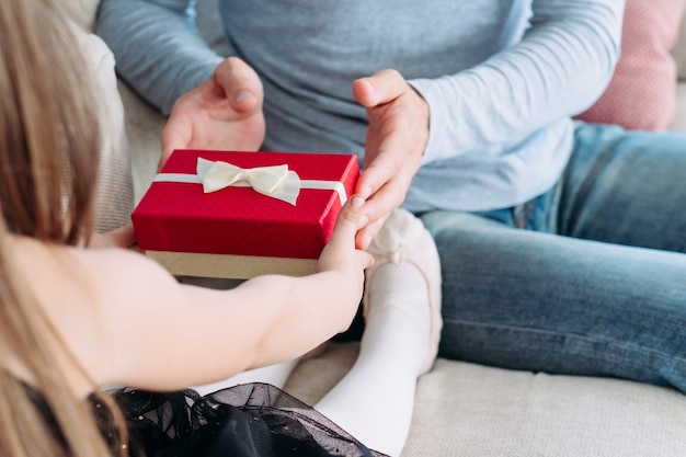 vader presenteert een geschenk aan zijn kleine jongen meisje in een rode doos. gelukkige jeugd en goed ouderschap.