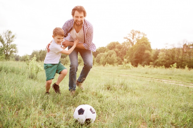 Vader speelt voetbal met zijn zoon. Ze rennen door de wei. De jongen koestert zijn vader en bekijkt bal. De mens doet hetzelfde.