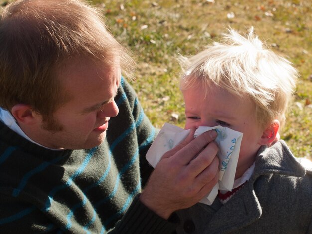 Vader veegt neus van zijn zoon af met tissue.