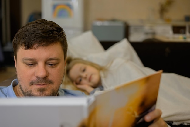 vader vermaakt het kind tijdens ziekte hij kijkt leest een boek een fotoboek met zijn dochter thuis