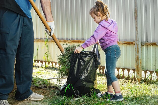 Vader verzamelt afval met een schop, een klein meisje helpt hem en houdt een vuilniszak vast