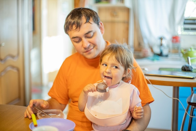 Vader voedende baby zittend op zijn handen thuis. alleenstaande vader. schattige peuter die ijs eet