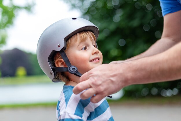 Vader zet een veiligheidshelm op lachende jongetje voor scooter, fietsen en skaten in het park