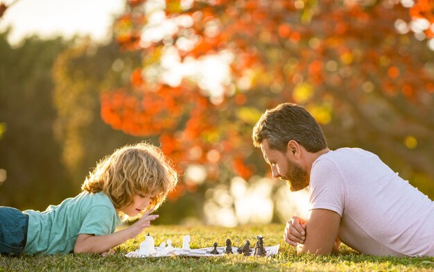 Vaderdag. gelukkig gezin. ouderschap en kindertijd. schaakmat. samen tijd doorbrengen. strategisch en tactisch. mentorschap. vader en kind spelen logisch spel. vader en zoon schaken op gazon.