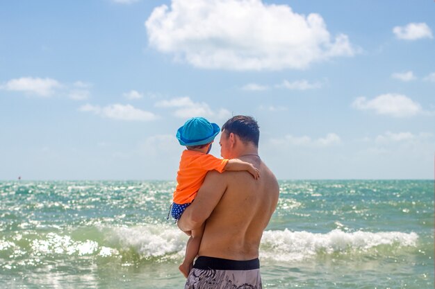 Vaderdag papa en baby in zijn armen kijken naar de golven van de zee