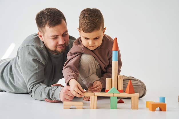 Vaderschap Zoon en vader spelen met gekleurde bakstenen speelgoed op witte achtergrond Vader zorgt voor zijn kind