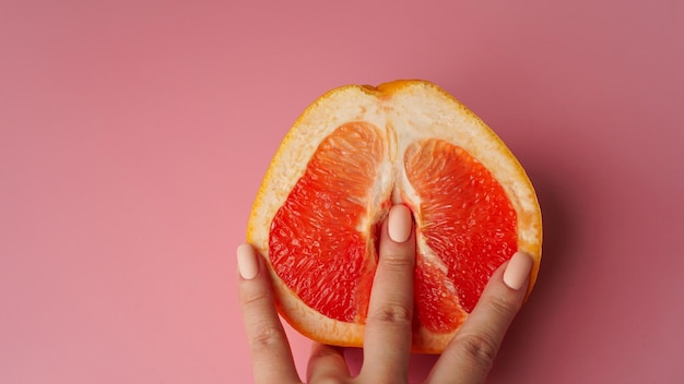 Vagina symbol. Fingers on grapefruit on pink background. Sex concept.