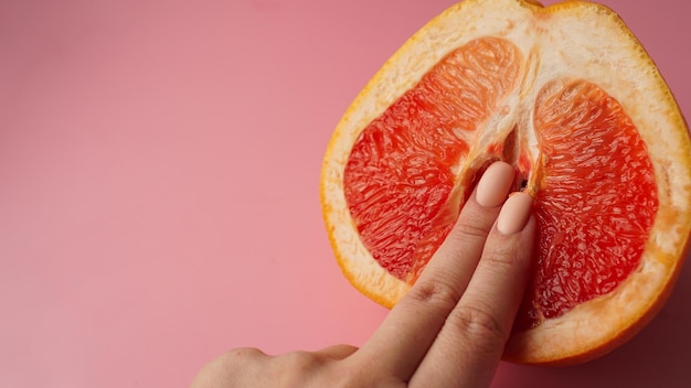 Photo vagina symbol. fingers on grapefruit on pink background. sex concept.