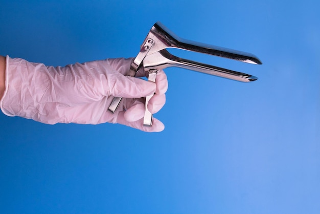 Vaginal speculum for examination by a gynecologist in the doctor's hand on a blue background