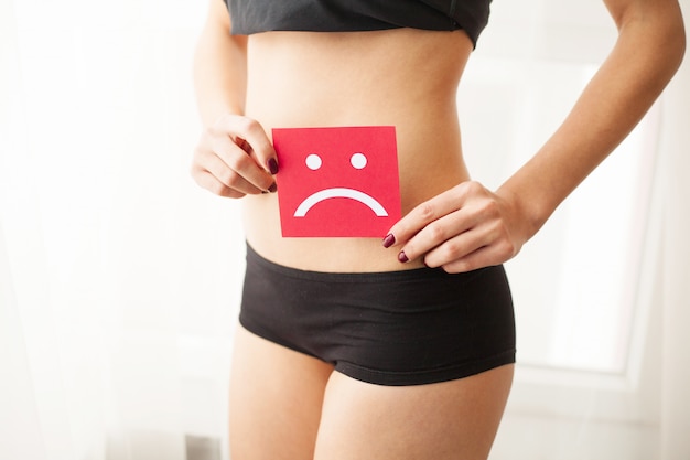 Vaginal or urinary infection and problems concept. young woman\
holds paper with sad smile above crotch