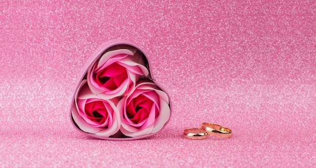 vak verrassingsgeschenk roze hart met gouden trouwringen met rozen op een glanzende achtergrond met bokeh voor Valentijnsdag