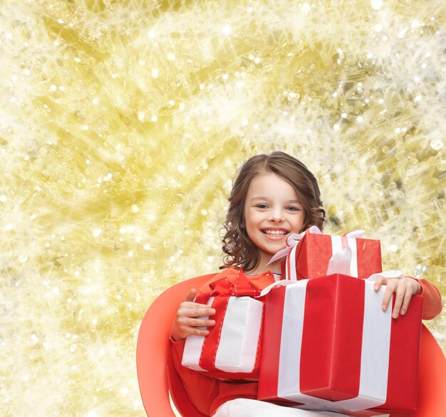 vakantie, cadeautjes, kerst, jeugd en mensen concept - glimlachend meisje met geschenkdozen over gele lichten achtergrond