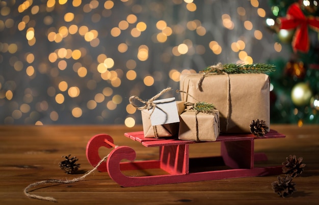 vakantie, cadeautjes, nieuwjaar en viering concept - close-up van geschenkdozen met lege notitie op rode houten slee over kerstboom en lichten achtergrond