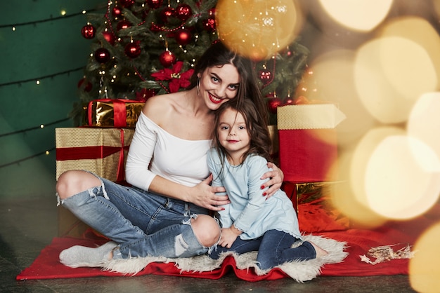 Vakantie conceptie. Vrolijke moeder en dochter zitten in de buurt van de kerstboom die erachter