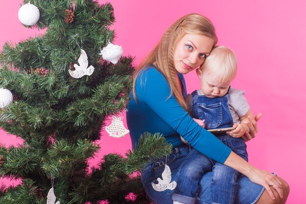 Vakantie en mensen concept - vrouw en haar kind in de buurt van kerstboom op roze ruimte