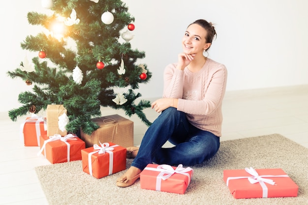 Vakantie, feest en feestelijk concept - Mooie jonge vrouw die onder de kerstboom zit