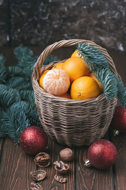 Vakantie-inhoud, mandarijnen, gepelde mandarijn in een rieten mand, vintage, vuren tak, kerstboom rode ballen, walnoot, donkerbruine achtergrond