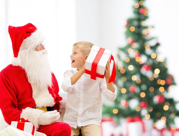 vakantie, jeugd en mensen concept - lachende kleine jongen met de kerstman en geschenken over kerstboom lichten achtergrond