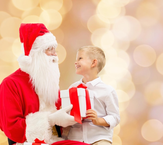 vakantie, Kerstmis, jeugd en mensen concept - lachende kleine jongen met de kerstman en geschenken over beige lichten achtergrond