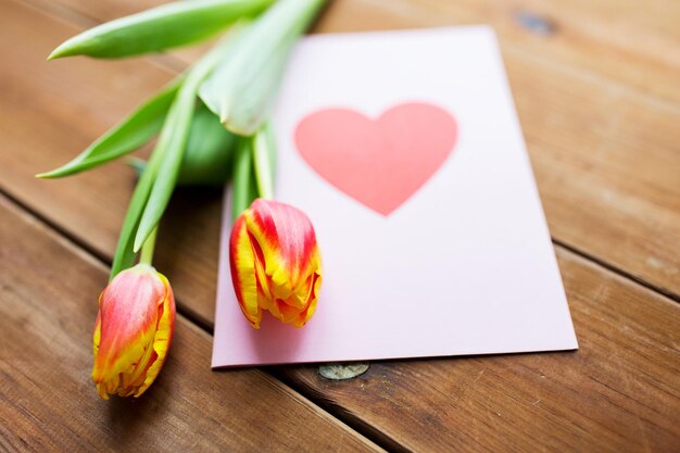 vakantie, liefde en valentijnsdag concept - close-up van tulp bloemen en wenskaart met hart op houten tafel