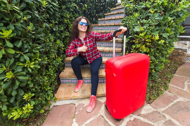 Vakantie, reizen, mensen concept - jonge vrouw in zonnebril zittend op trappen met koffers en glimlachen.