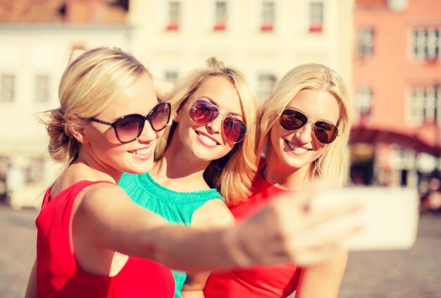 vakantie, toerisme en modern technologieconcept - lachende meisjes die foto's maken met smartphonecamera in de stad