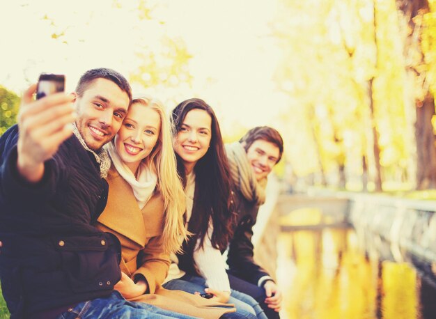 vakantie, vakantie, reizen en toerisme concept - groep vrienden of koppels die plezier hebben in het herfstpark en selfie nemen