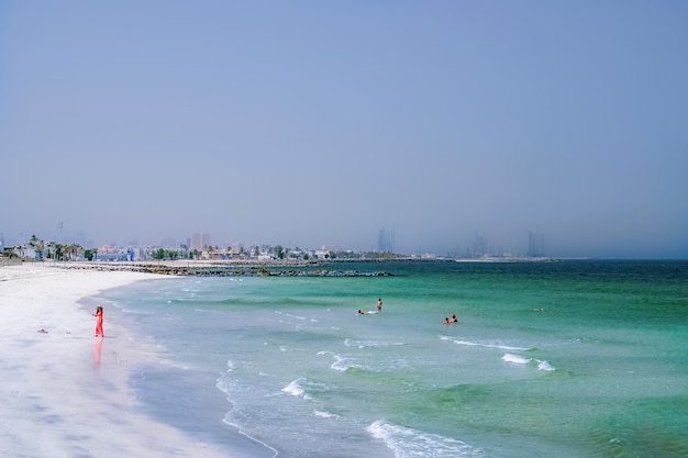 Vakantie vakantie strand achtergrond. Dubai. De Perzische Golf met de lijn van het strand van de Ajman. Vrouw in rode spelen op het strand.