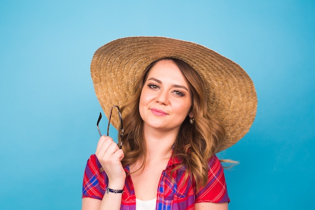 Vakantie, zomer, mode en mensen concept - meisje in modieuze kleding strohoed. Portret van charmante vrouw op blauwe achtergrond met lege kopie ruimte.