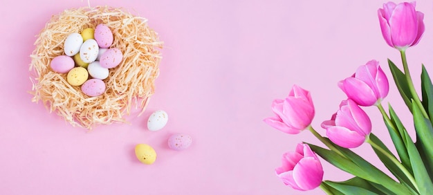 Vakantieachtergrond Gekleurde paaseieren in een nest van stro en tulpen op de roze achtergrond Kopieer ruimte