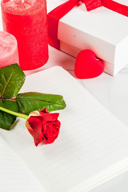 Vakantieachtergrond, Valentijnsdag. Boeket rode rozen, stropdas met een rood lint, met blocnote, gewikkelde geschenkdoos en rode kaars. Op een witte marmeren tafel