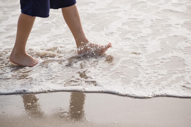 Vakantieconcept close-up van jongensbenen die op het water aan het strand lopen