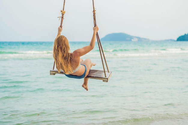 Vakantieconcept. Gelukkig jonge vrouw zittend op de schommel genieten van uitzicht op zee