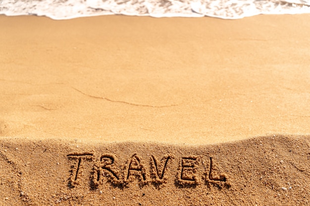 Vakantieconcept op het strand. Word Travel geschreven op het zand in de buurt van de zee.