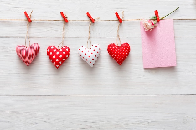 Valentijn met rode papieren harten rij grens op wasknijpers en papieren kaart met roze bloem op rustieke houten planken