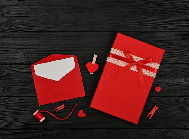 Foto valentijngeschenken voorbereiden, rode dozen, harten, touw, wasknijpers en notitie in papieren envelop op zwarte houten tafel achtergrond, close-up plat leggen, verhoogde bovenaanzicht, direct erboven