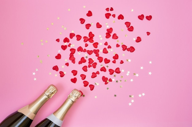 Valentijnsdag achtergrond. Champagne-flessen, rode harten en gouden confettien op roze achtergrond.