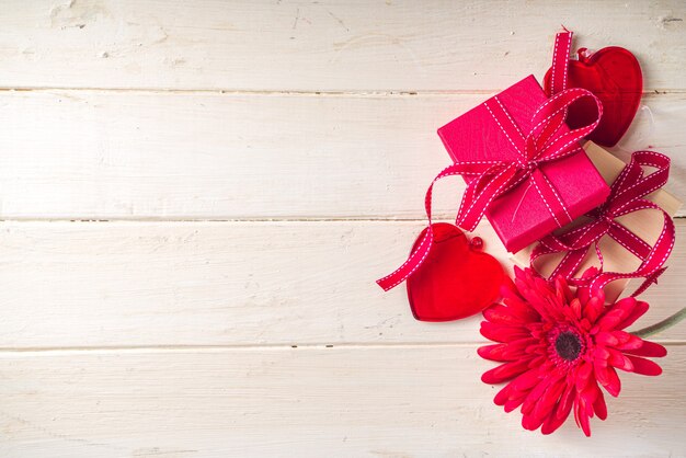 Valentijnsdag achtergrond. Geschenkdozen met feestelijk lint, glas rood hart en rode gerberabloem op lichte houten achtergrond. kopieer ruimte voor uw tekst