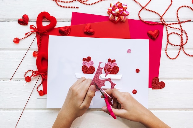 Valentijnsdag achtergrond. Handgemaakte cadeau-wenskaart maken, knippen en plakken, ambachtelijk papier, vilt en doe-het-zelf gereedschap op wit hout. Bovenaanzicht, plat gelegd