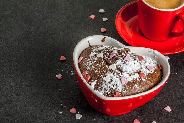 Valentijnsdag achtergrond, rode koffiemok en chocolademok cake of brownie met poedersuiker en zoete hartvormige hagelslag, zwarte achtergrond, kopie ruimte