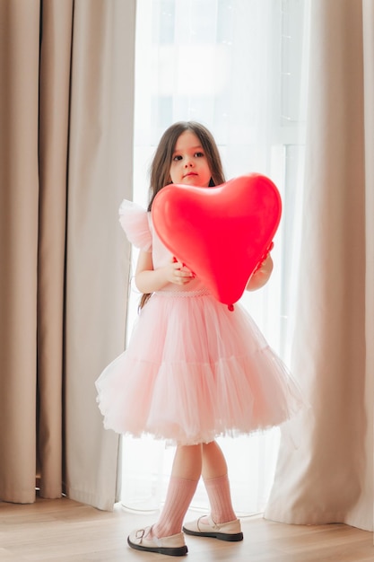 Valentijnsdag baby Een klein meisje in een rode jurk houdt een grote bal vast in de vorm van een hart