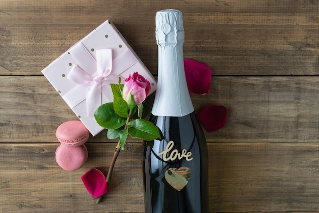 Valentijnsdag. Champagnefles met LOVE inscriptie op de fles. Geschenkdoos met een roos op een houten ondergrond. Ruimte kopiëren. Bovenaanzicht.