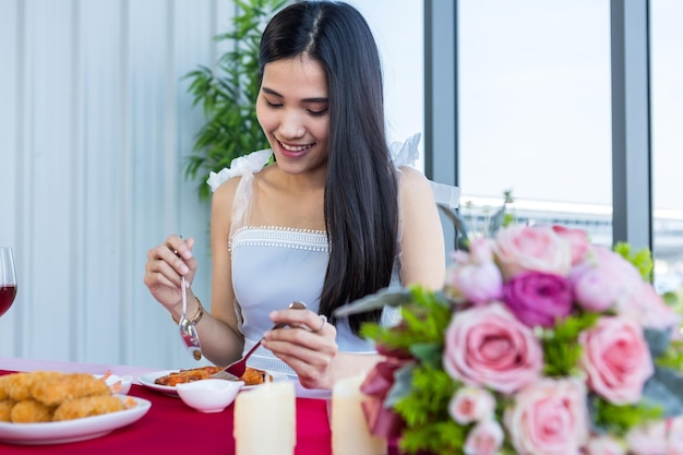 Valentijnsdag concept Aziatisch jong meisje zittend aan een tafel eten met wijnglazen en boeket van rode en roze rozen wijn en wachten op haar man op in de achtergrond van het restaurant