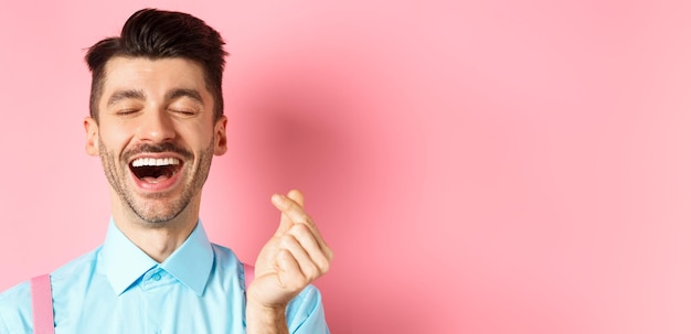 Valentijnsdag concept gelukkige man verliefd vinger hart tonen en lachen staande op romantisch roze