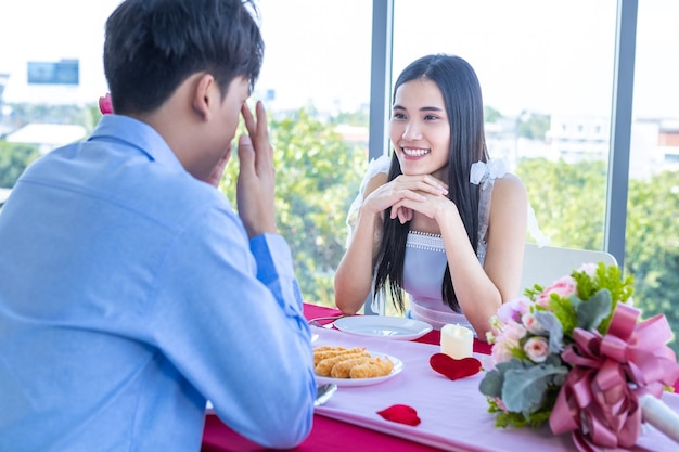 Valentijnsdag concept, happy asian young sweet couple met romantisch de lunch met een boeket rozen op de achtergrond van het restaurant.