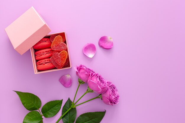 Valentijnsdag concept. Roze doos met marmelade en bitterkoekjes en een mooie roos op een roze tafel